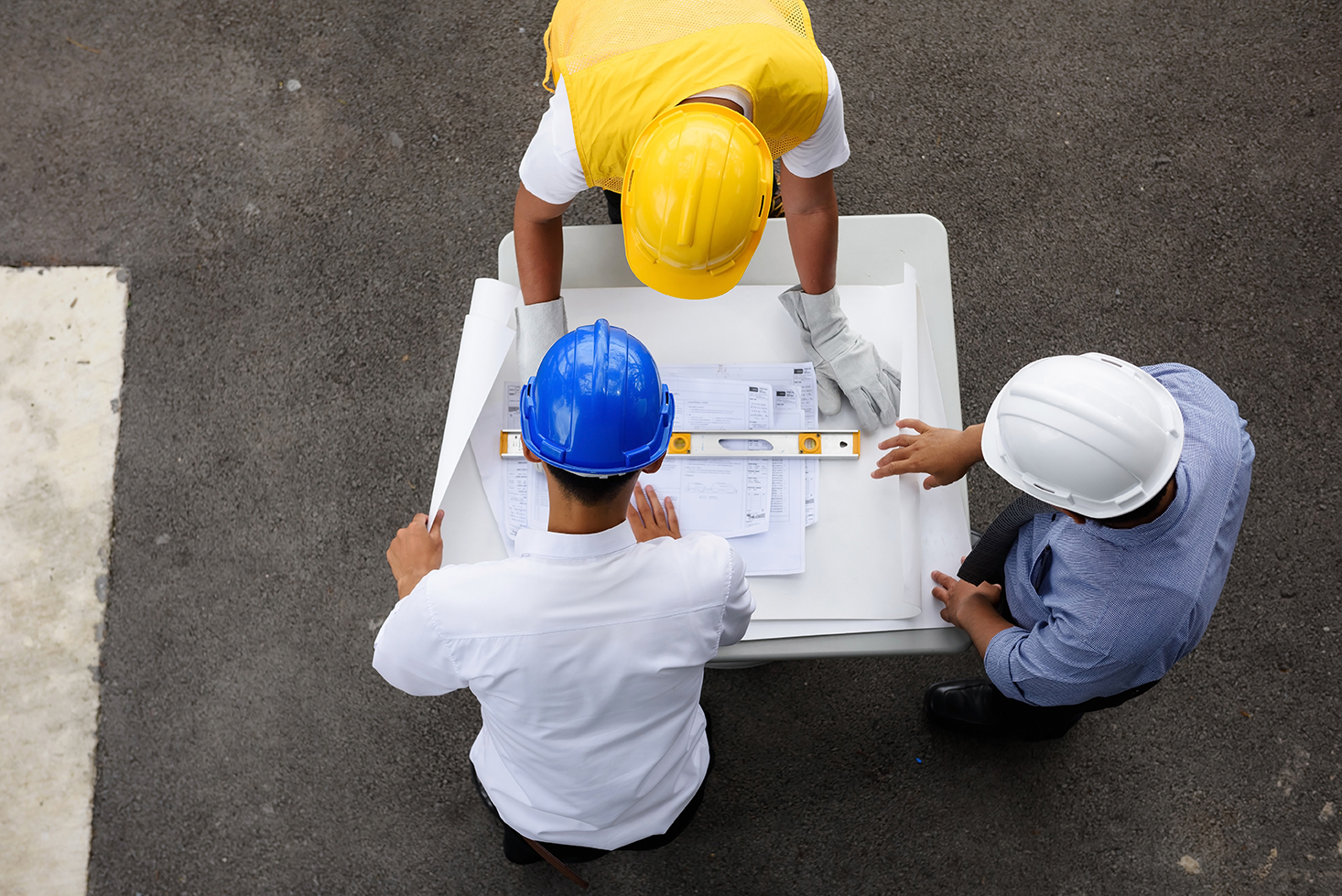 Top view of engineering team of site manager, field engineer and foreman looking at  constructed paper blueprint plans at construction site. Business Concept for team work of heavy industry.