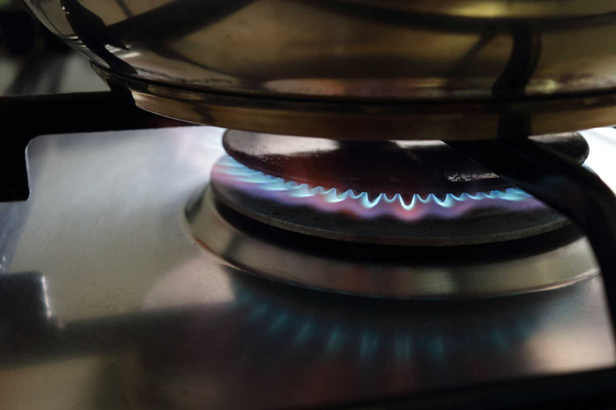 Cooker (household, home, domestic appliance) on propane butane (liquefied or liquid petroleum gas) burn with blue flame and on grille is metal pot from dishware. LP gas is economic fuel for cooking.