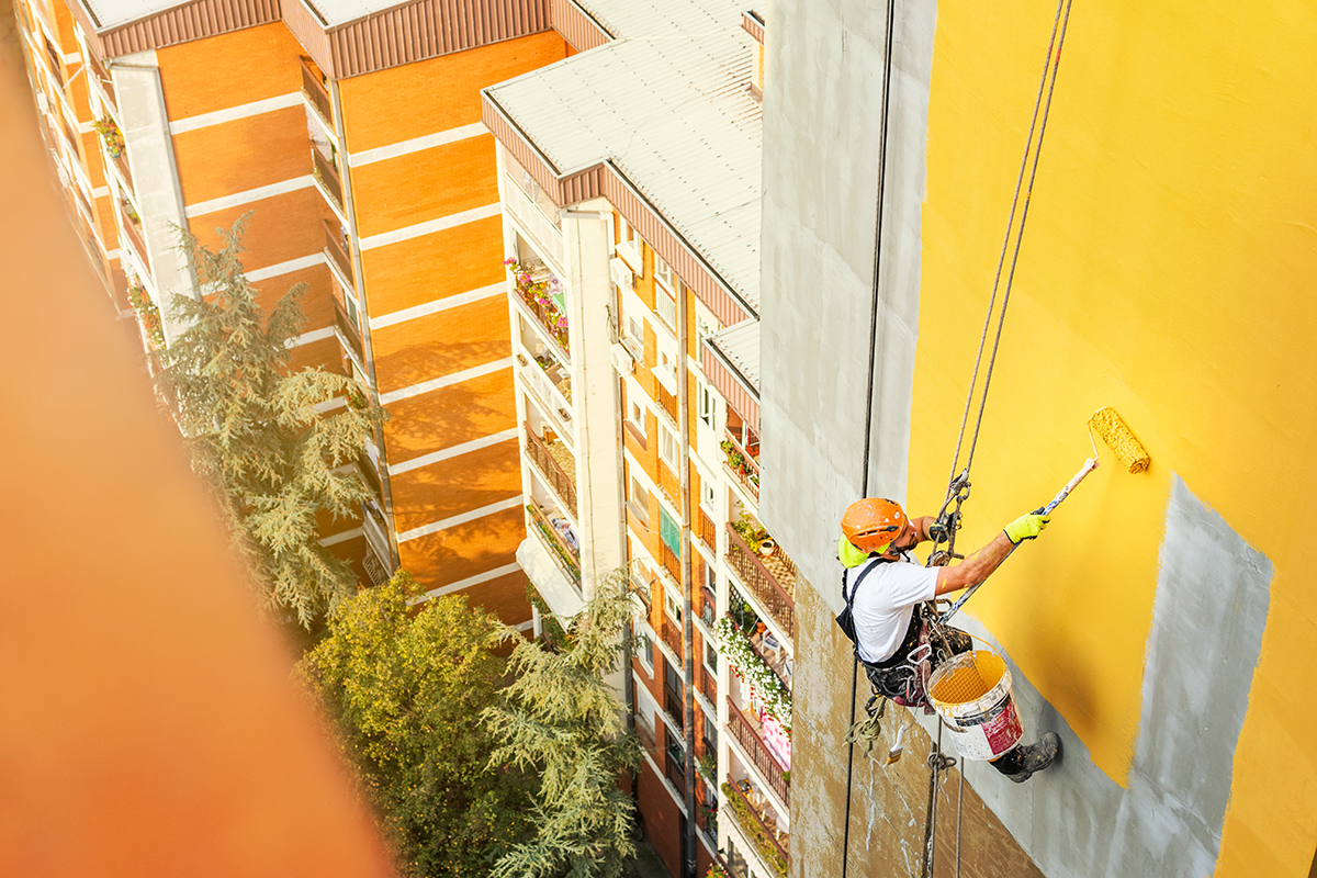 Pintor recubriendo el exterior de un edificio con pintura amarilla